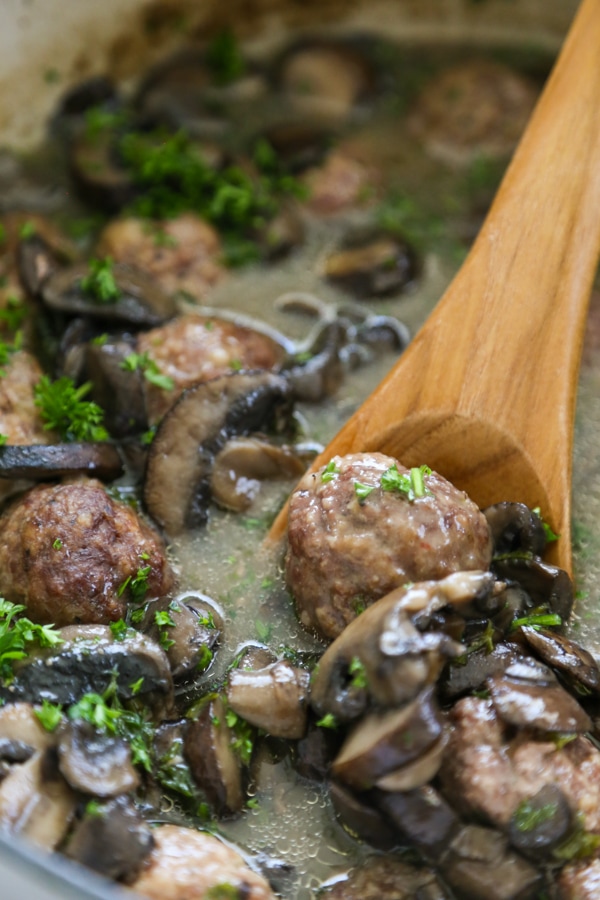 marsala meatballs and mushrooms in a pan with a wooden spoon.