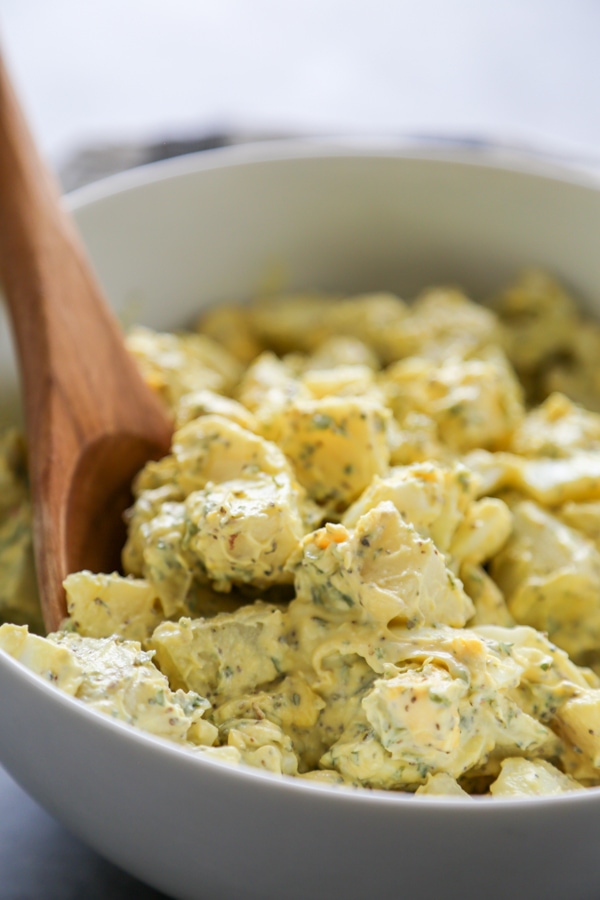 a bowl of potato salad with a wooden spoon.