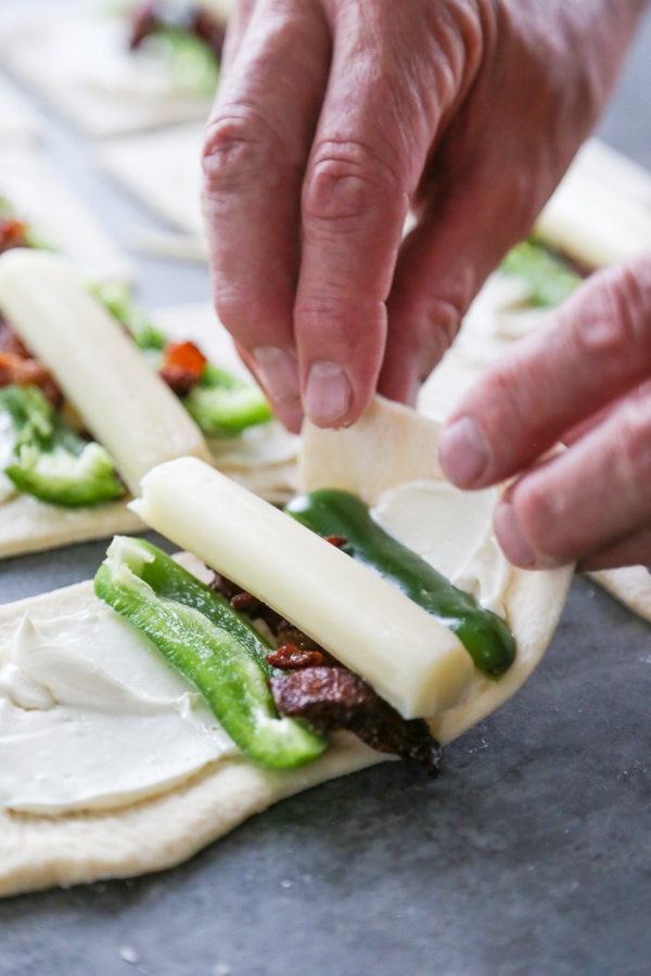 dough being rolled up with cheesestick, peppers, and bacon.