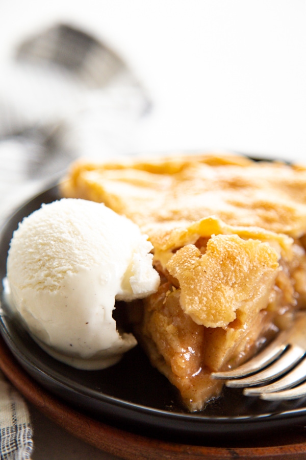 slice of apple pie on a black plate with scoop of vanilla ice cream