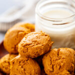 pumpkin cookies stacked on wood plate with glass of milk