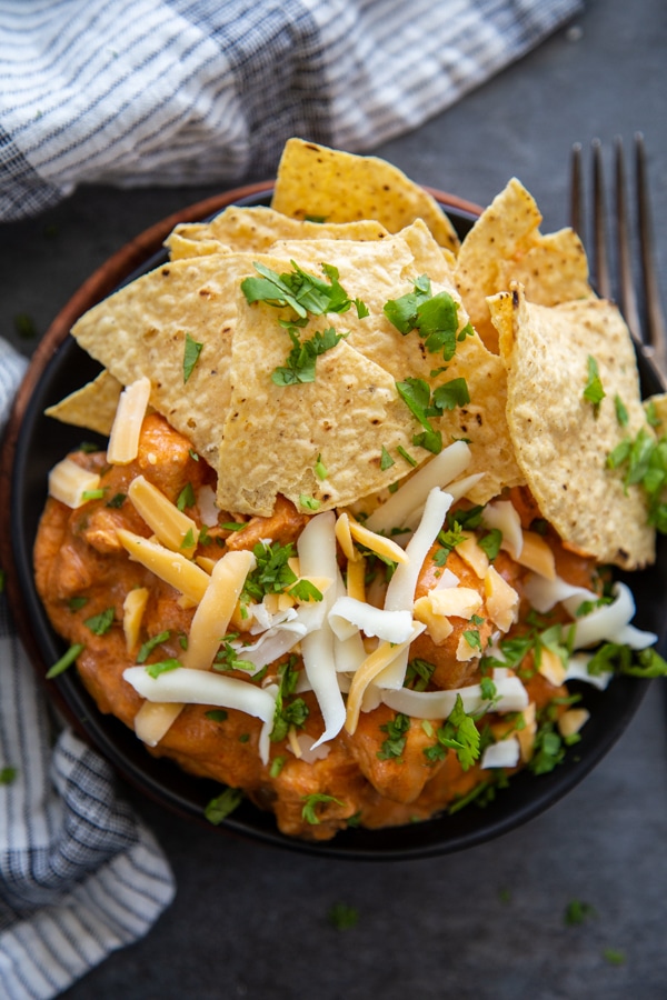 top view chicken nachos with chips, cilantro and cheese on black plate