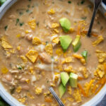 overhead shot of white chicken chili in bowl with chopped avocados and chips
