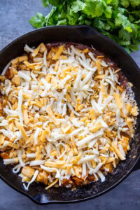 grated cheese over chicken in skillet
