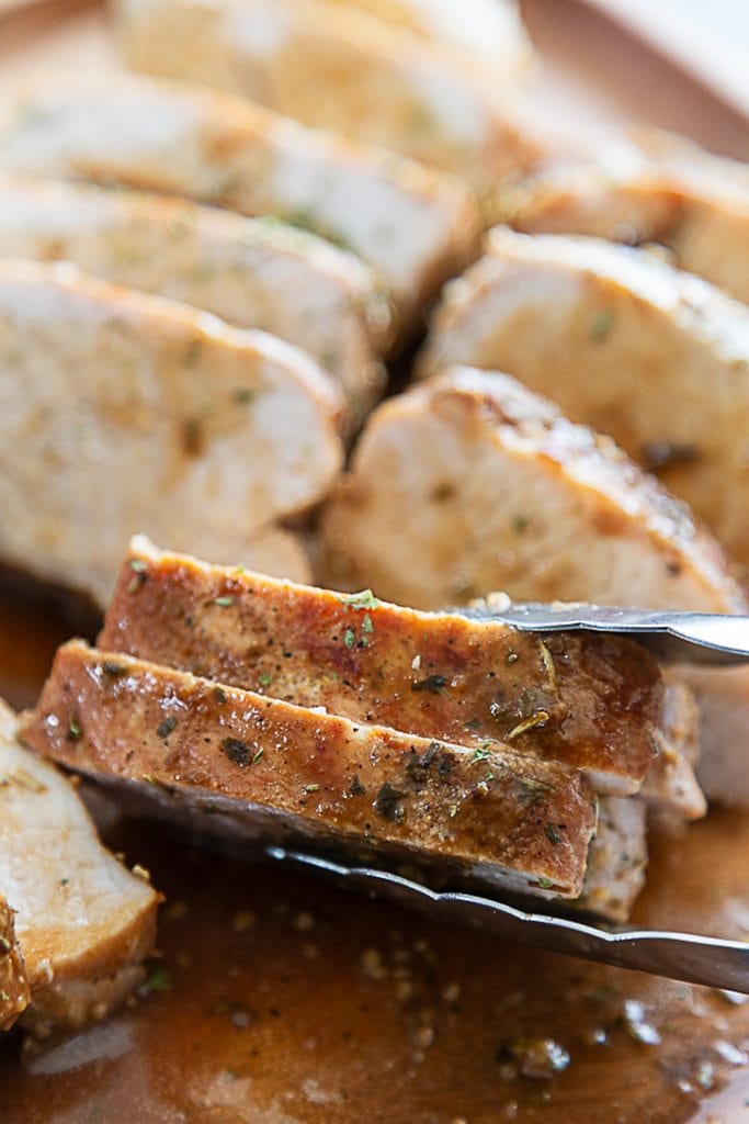 tongs grabbing pork tenderloin sliced