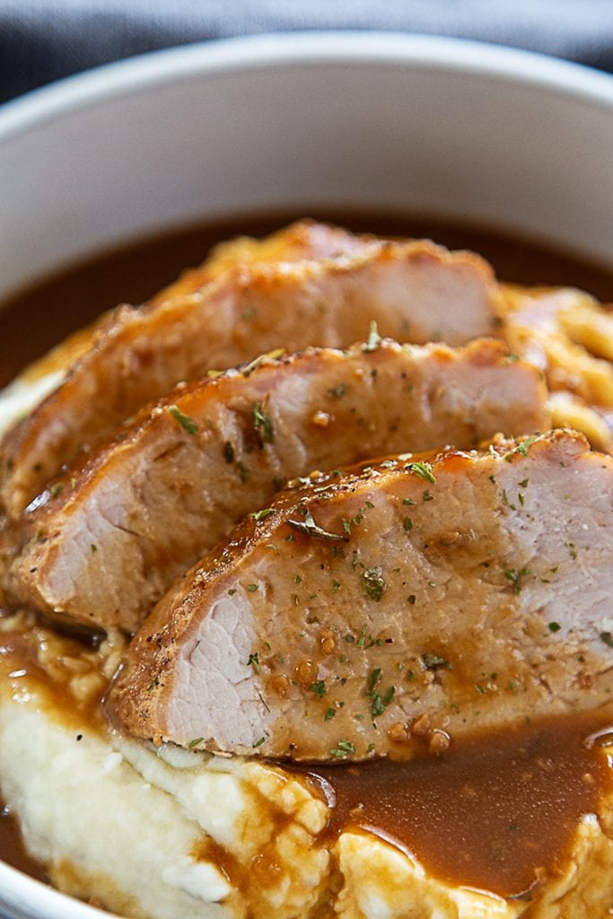 close up shot pork tenderloin over mashed potatoes and gravy