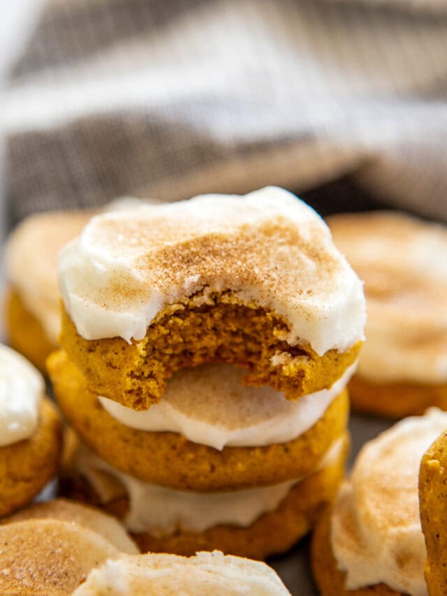 stack of frosted pumpkin cookies with bite out of top one